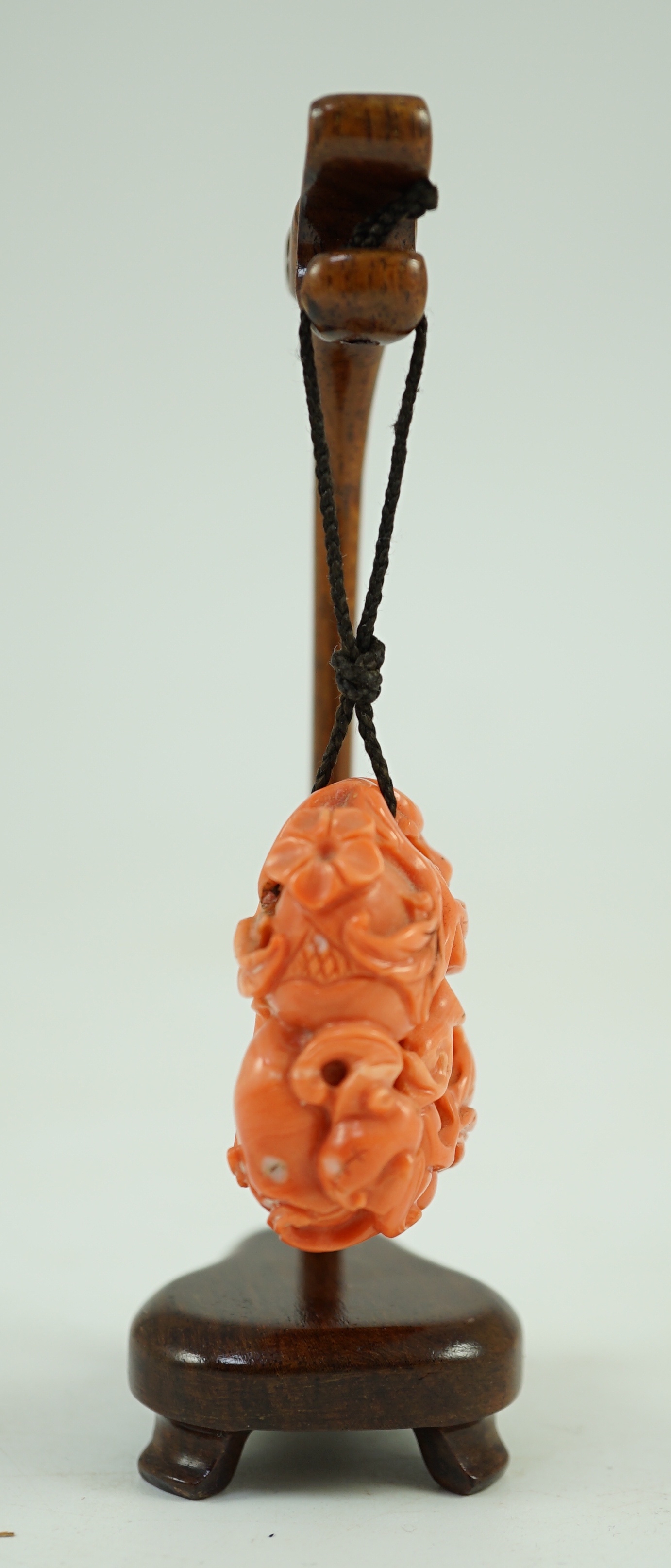 A good Chinese coral ‘fruit and bats’ pendant, 19th century, 3.7cm, later suspension stand